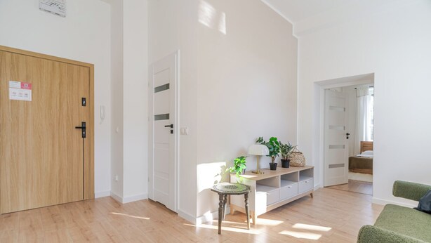 Amplia sala de estar con piso de madera, un sofá verde, una mesita con una lámpara y una planta en maceta.