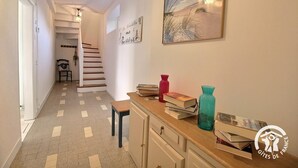 A hallway with a staircase, a bench, a desk with books and vases, and a framed picture on the wall. - Les Hirondelles - LAURENAN (LAURENAN)