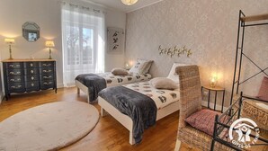 A bedroom with two beds, a dresser, a chair, and a hanging light fixture. - Les Hirondelles - LAURENAN (LAURENAN)