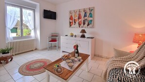 A cozy living room with a wooden coffee table, a white sofa, a striped chair, a TV mounted on the wall, and a painting above the sofa. - Les Hirondelles - LAURENAN (LAURENAN)