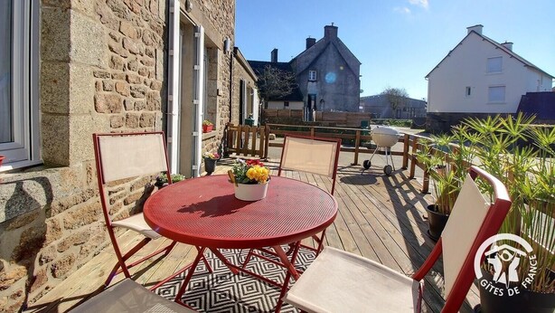 A patio with a red metal table and chairs, a potted plant, and a barbecue grill. - Les Hirondelles - LAURENAN (LAURENAN)