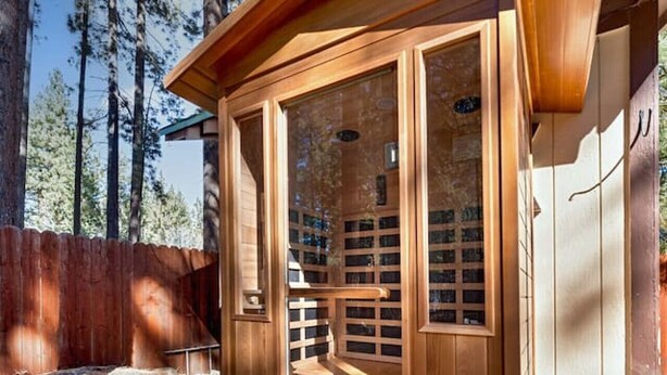 Eine Holzhütte für die Sauna mit Glastür, einer Holzterrasse und einem umgebenden Holzzaun.