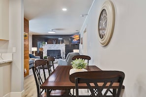 A dining area with a wooden table and chairs, a fireplace, and a television in the background. - Tahoe Pines Cabin | Sauna + Shuttle + EV (South Lake Tahoe)