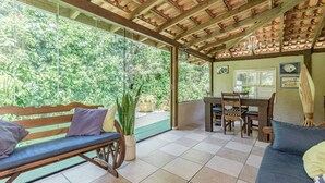 A covered patio with a wooden bench, a dining table with chairs, and a sofa. - Casa em Condom nio com Piscina e rea Gourmet (Garopaba)