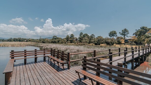 A wooden deck with benches overlooking a calm body of water, surrounded by trees and a clear sky. - Casa em Condom nio com Piscina e rea Gourmet (Garopaba)