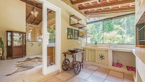 A rustic kitchen with a wooden cart, a large window with a view of greenery, and a traditional cabinet. - Casa em Condom nio com Piscina e rea Gourmet (Garopaba)