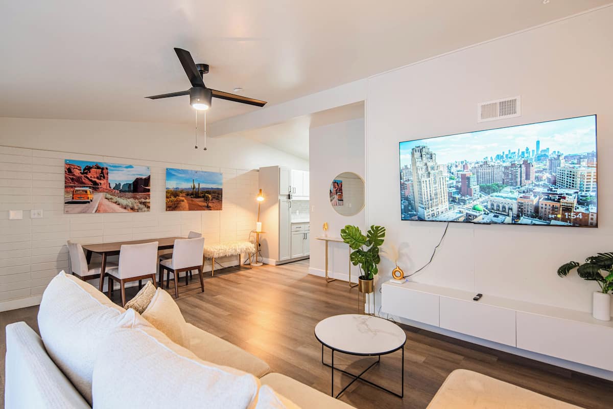 A modern living room with a large flat-screen TV, a ceiling fan, and a dining area with a table and chairs.