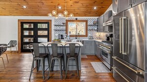 A modern kitchen with a wooden ceiling, stainless steel appliances, and a central island with bar stools. - Blue Ridge Retreat - Lakefront | Dock | Firepit | Game Room (Blue Ridge)