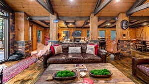 A cozy cabin interior with a stone fireplace, leather furniture, and a dining area. - Big Bear Falls - Riverfront | Pet Friendly | Hot Tub (Ellijay)