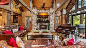 A spacious living area with a stone fireplace, leather furniture, and a piano. - Big Bear Falls - Riverfront | Pet Friendly | Hot Tub (Ellijay)