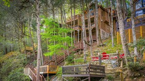 A multi-level wooden cabin with wooden railings and stairs, surrounded by trees. - Big Bear Falls - Riverfront | Pet Friendly | Hot Tub (Ellijay)