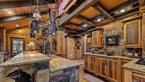A rustic kitchen with stone countertops, wooden cabinets, and hanging cookware. - Big Bear Falls - Riverfront | Pet Friendly | Hot Tub (Ellijay)