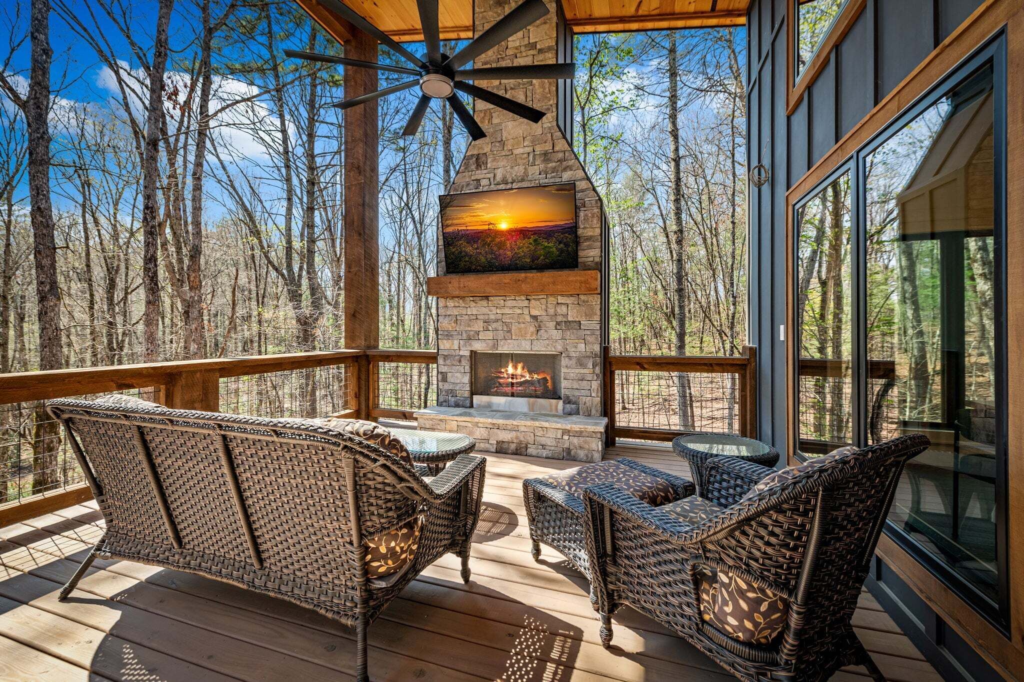 A deck with wicker furniture, a stone fireplace, and a view of the forest.