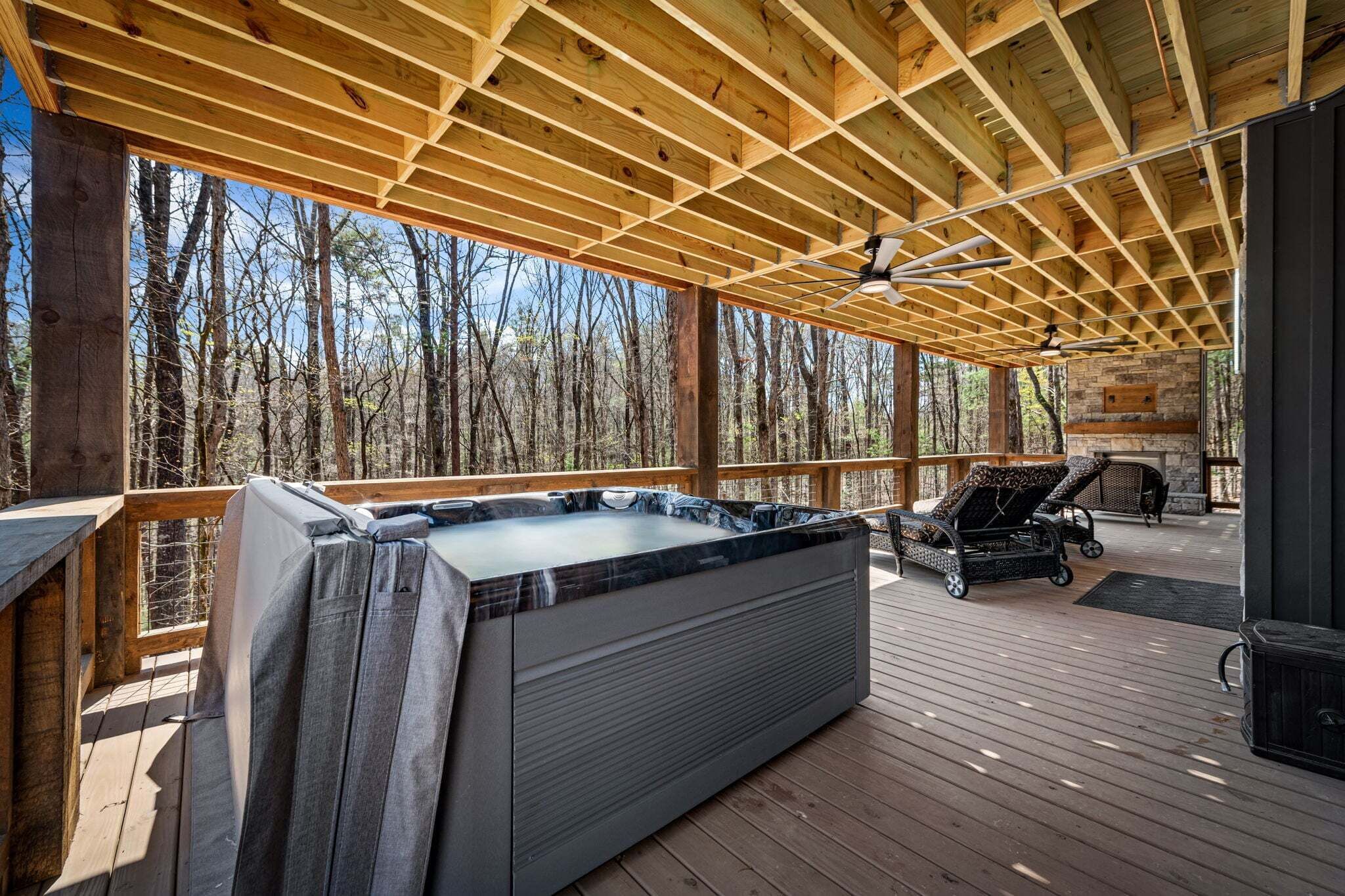Une terrasse en bois avec un jacuzzi, des chaises longues et une cheminée en pierre.