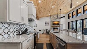 Una cucina moderna con mobili bianchi, un piano di lavoro in marmo, soffitto in legno e ampie finestre.