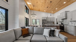 Una cucina moderna con mobili bianchi, soffitto in legno e un divano modulare grigio con cuscini.