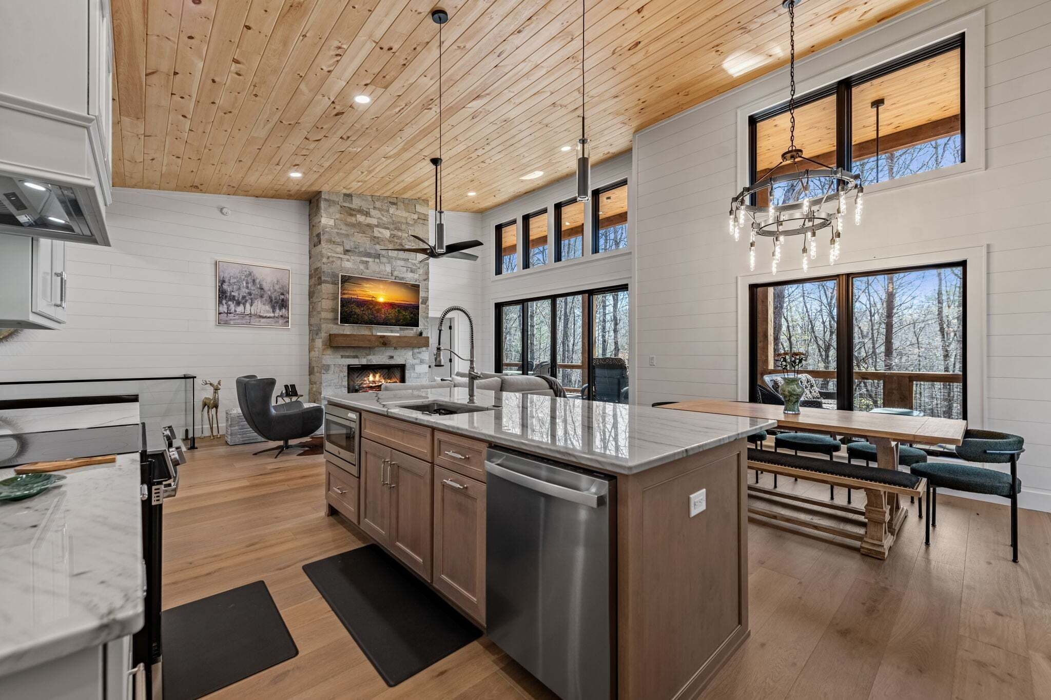 A modern kitchen with a large island, wooden ceiling, and large windows.