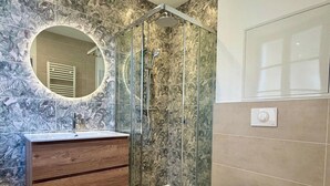 Ein Badezimmer mit Marmor-Spritzschutz, einem Holzbadezimmermöbel, einer Duschkabine aus Glas und einer Toilette.