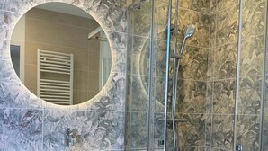 Ein modernes Badezimmer mit einer in Glas eingefassten Dusche, einem hölzernen Waschtisch mit rundem Spiegel und einer gefliesten Wand mit floralem Muster.