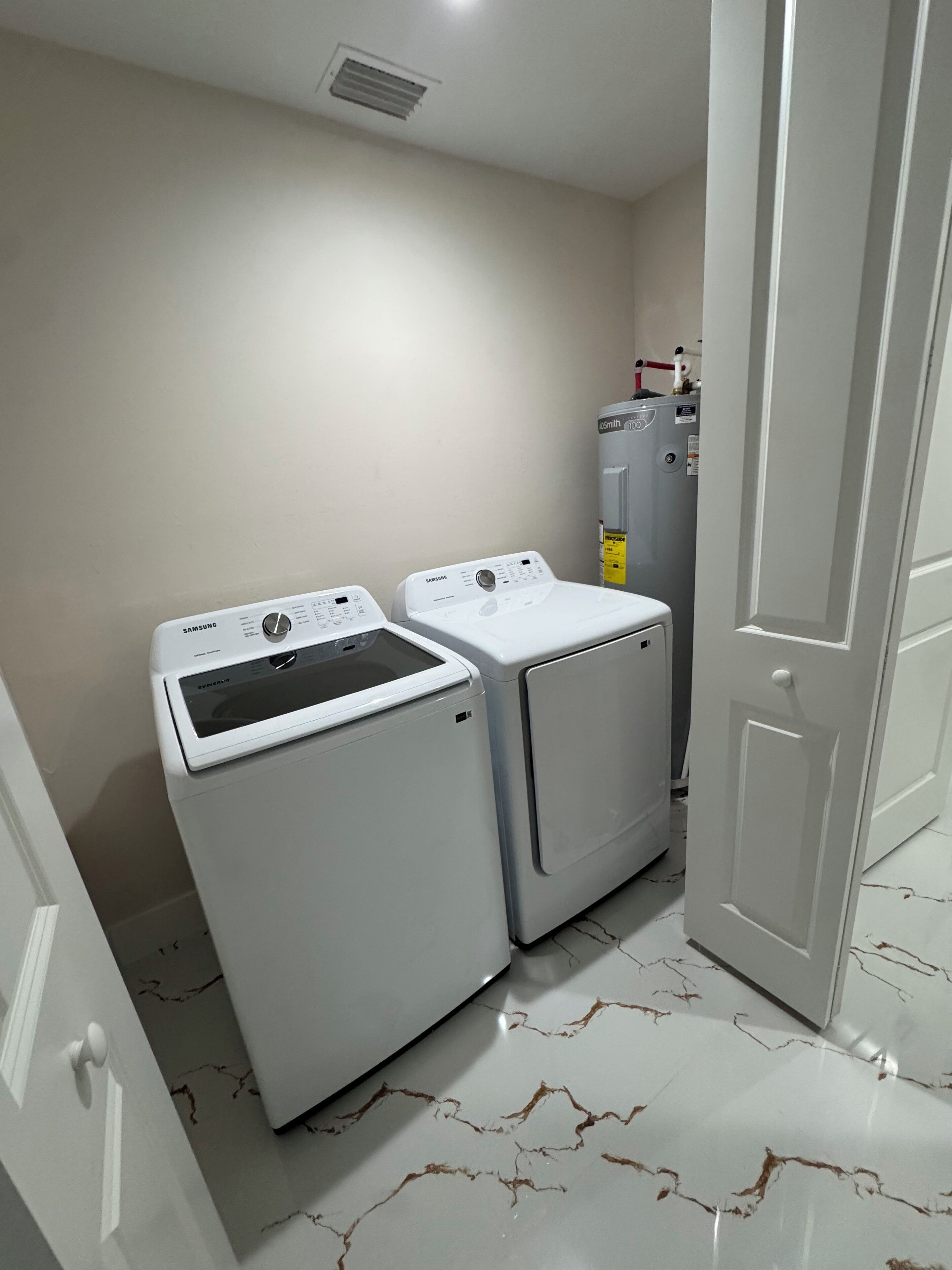 A laundry room with two white washing machines and a water heater.