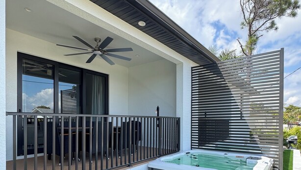 Ein moderner Außenbereich mit Whirlpool, Kunstgrras, einem Balkon mit Deckenventilator und einer Pergola.