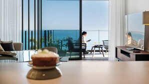 A modern hotel room with a balcony overlooking the sea, a dining area with a table and chairs, and a TV on a stand. - III - Savoy Monumentalis, By Pausa Holiday Rentals (Funchal)