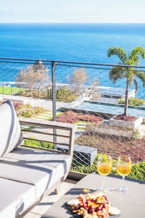Une terrasse avec vue sur l’océan, une table à manger dressée avec de la nourriture et des boissons, et un fauteuil de relaxation.