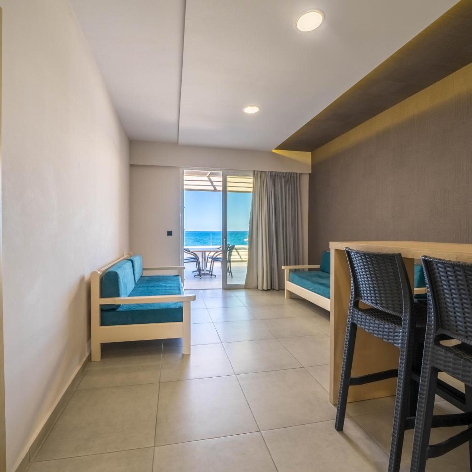A hotel room with a balcony, a sofa, a bed, and a table with chairs.