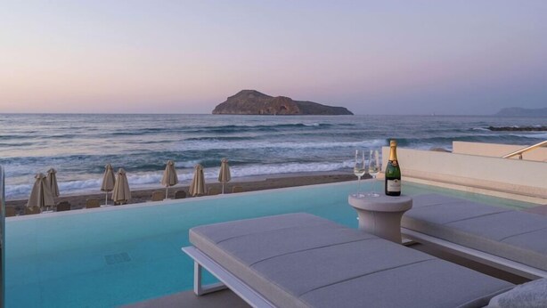 A poolside area with lounge chairs and umbrellas, overlooking the ocean with a view of a small island. - Marika Hotel Chania (Platanias)