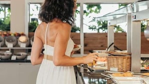 A woman in a white dress serving food at a buffet with a modern interior and wooden accents. - Marika Hotel Chania (Platanias)