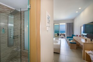 A modern hotel room with a glass-enclosed shower, a seating area with a view of the sea, and a flat-screen TV. - Marika Hotel Chania (Platanias)