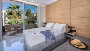 A modern hotel room with a large bed, a desk with chairs, a balcony with palm trees, and a view of other buildings. - Marika Hotel Chania (Platanias)
