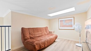 Ein Zimmer mit einem braunen Sofa, einem Deckenventilator, einem gerahmten abstrakten Gemälde und einem Holzboden.