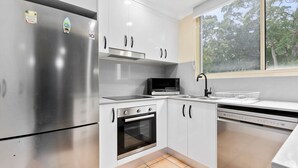 Una cucina moderna con elettrodomestici in acciaio inossidabile, mobili bianchi e una finestra che offre vista sugli alberi.