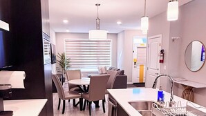 A modern kitchen with a central island, a dining area with chairs, a built-in oven, and a sink with a dish rack. - The Luxe Haven S - Luxury 3BR | 2.5BA Family Home • Stylish • Serene (Calgary)