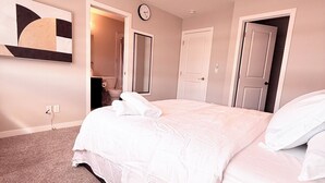 A bedroom with a bed, a clock, and a door leading to another room. - The Luxe Haven S - Luxury 3BR | 2.5BA Family Home • Stylish • Serene (Calgary)