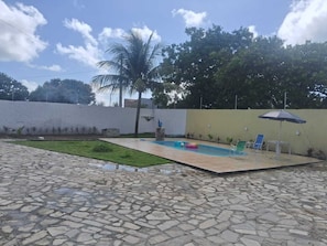 A swimming pool with a stone-tiled deck, a palm tree, and a white wall.