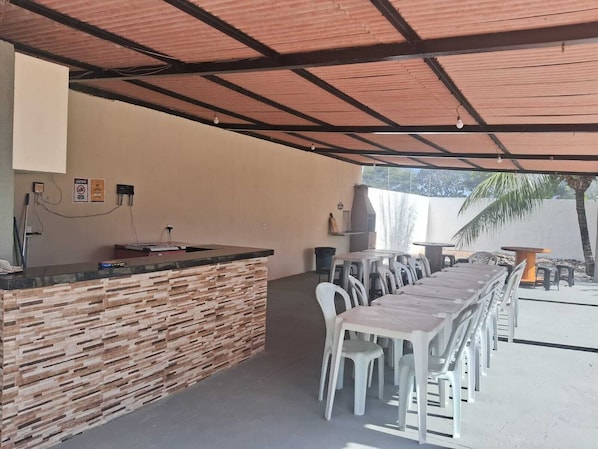 An outdoor patio with a stone counter, white plastic chairs, and a grill.