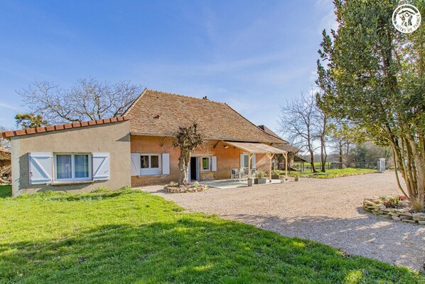 Uma casa de dois andares com telhado de telhas, varanda coberta e entrada com calçamento de brita.