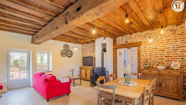 A cozy living room with a red sofa, a wooden dining table, and a brick wall. - Cosy Bresse - SAINT VINCENT EN BRESSE (SAINT VINCENT EN BRESSE)