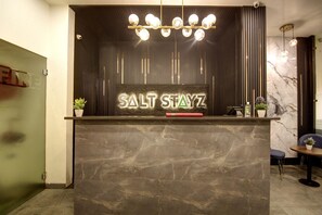 A reception desk with a sign that reads 'SALT STAYZ,' a potted plant, a red object, and a marble wall. - Saltstayz Thyme (New Delhi)