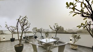 En tagterrasse med et rundt bord og stole, plantekasser og udsigt over bybilledet.