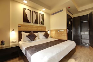 Una habitación de hotel con cabecera de madera, una cama grande con ropa de cama blanca y marrón, una mesita de noche con lámpara, y una obra de arte colgada en la pared.