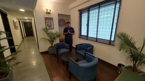 A hallway with a reception desk, two blue chairs, a small table, and potted plants. - Saltstayz Thyme (New Delhi)