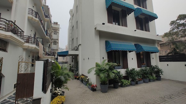 Un edificio residencial de varios pisos con balcones, plantas en macetas y una entrada portonada.