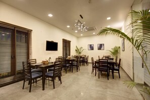 A conference room with multiple tables and chairs, a flat-screen TV, ceiling lights, and potted plants. - Saltstayz Thyme (New Delhi)