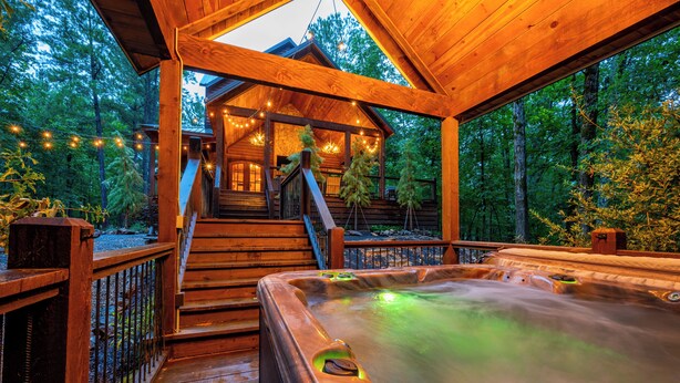 Een houten terras met een jacuzzi, houten trappen die naar een blokhut leiden, en lichtslingers.