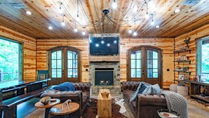 Een chaletinterieur met een stenen openhaard, leren banken, een houten bijzettafeltje en een groot raam.