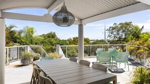 Patio esterno con tavolo e sedie, circondato da un parapetto bianco e da una rigogliosa vegetazione.