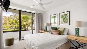 Una camera da letto moderna con un letto grande, due comodini, una ventola a soffitto e vista sul verde circostante.